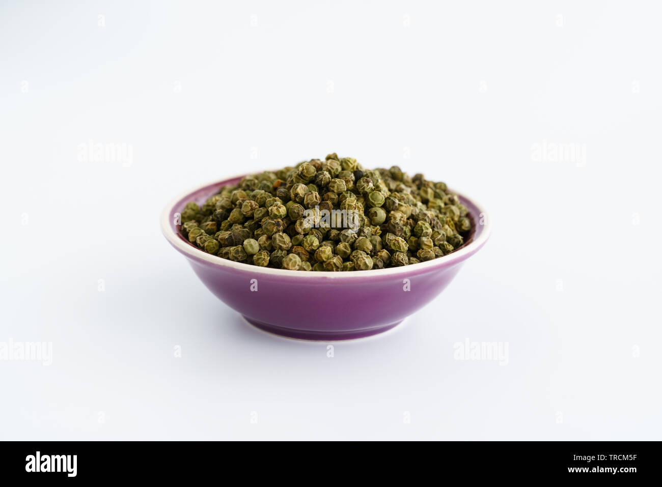 Dried green peppercorns in a violet bowl. White background, high