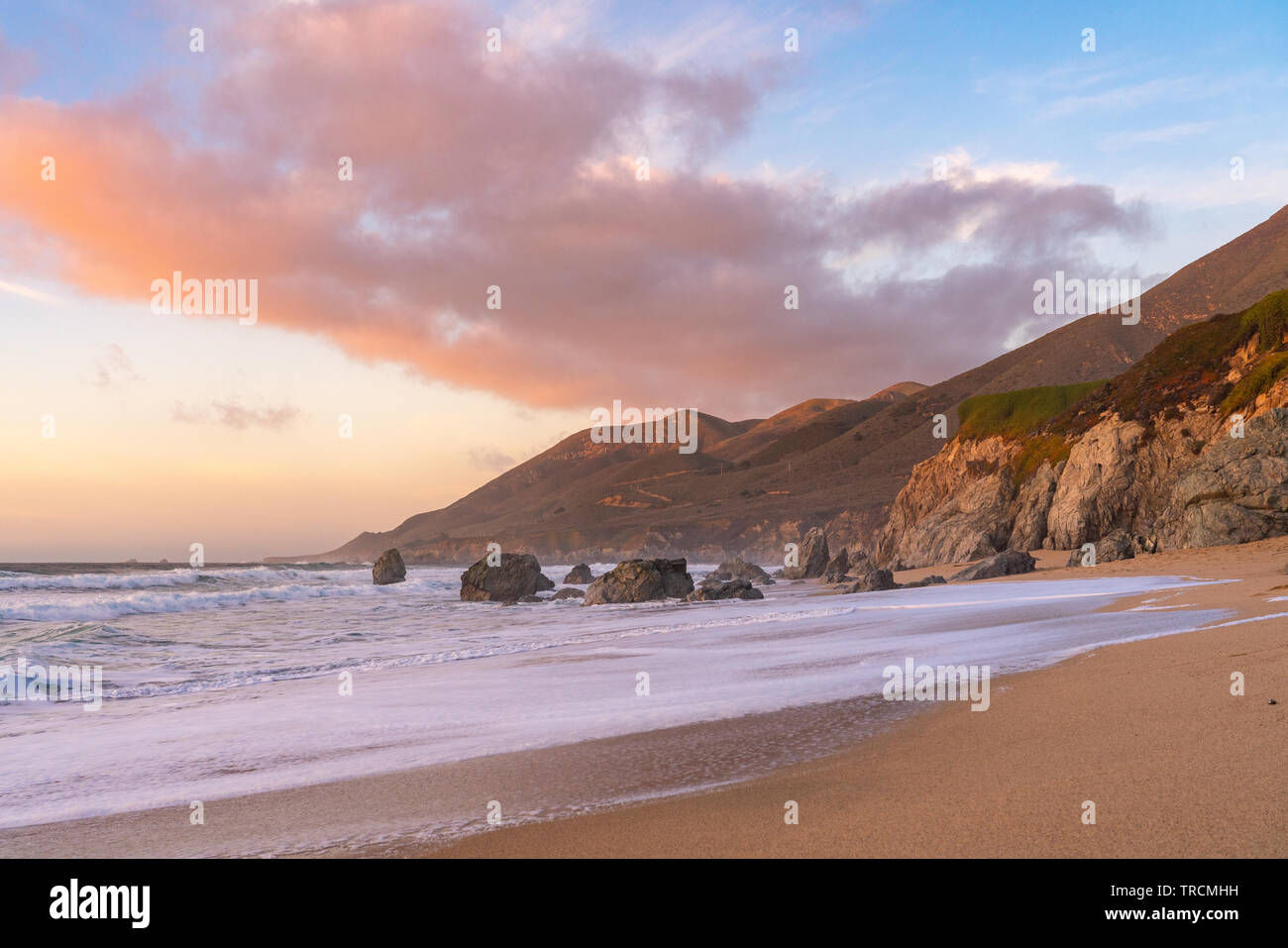 Sunset along a sandy beach with mountains in the along the coast in Big Sur, California. Stock Photo
