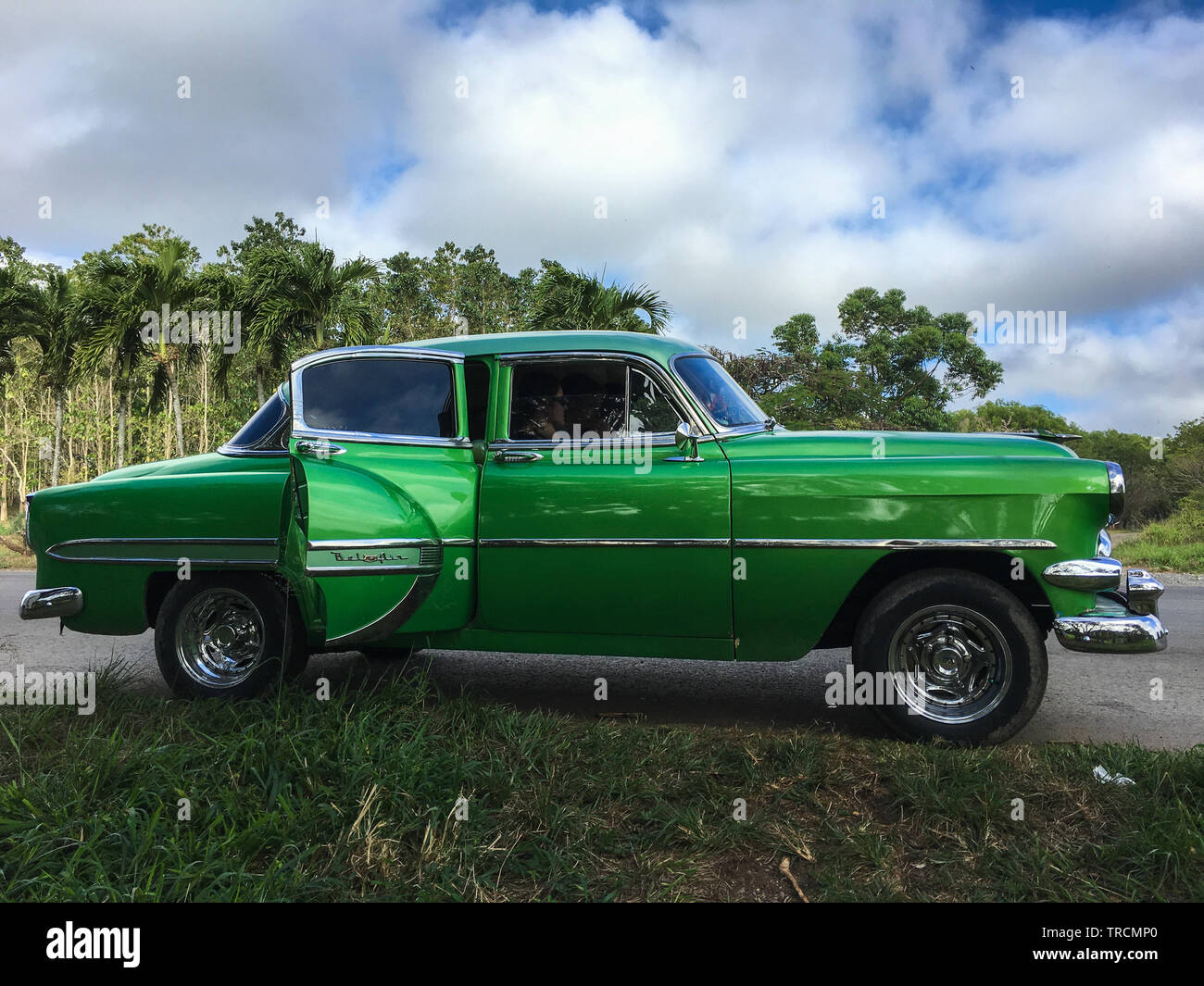 Classic green vintage American car stands parked on a road in front of some palm trees in the Vinales valley, Pinar Del Rio, Cuba Stock Photo