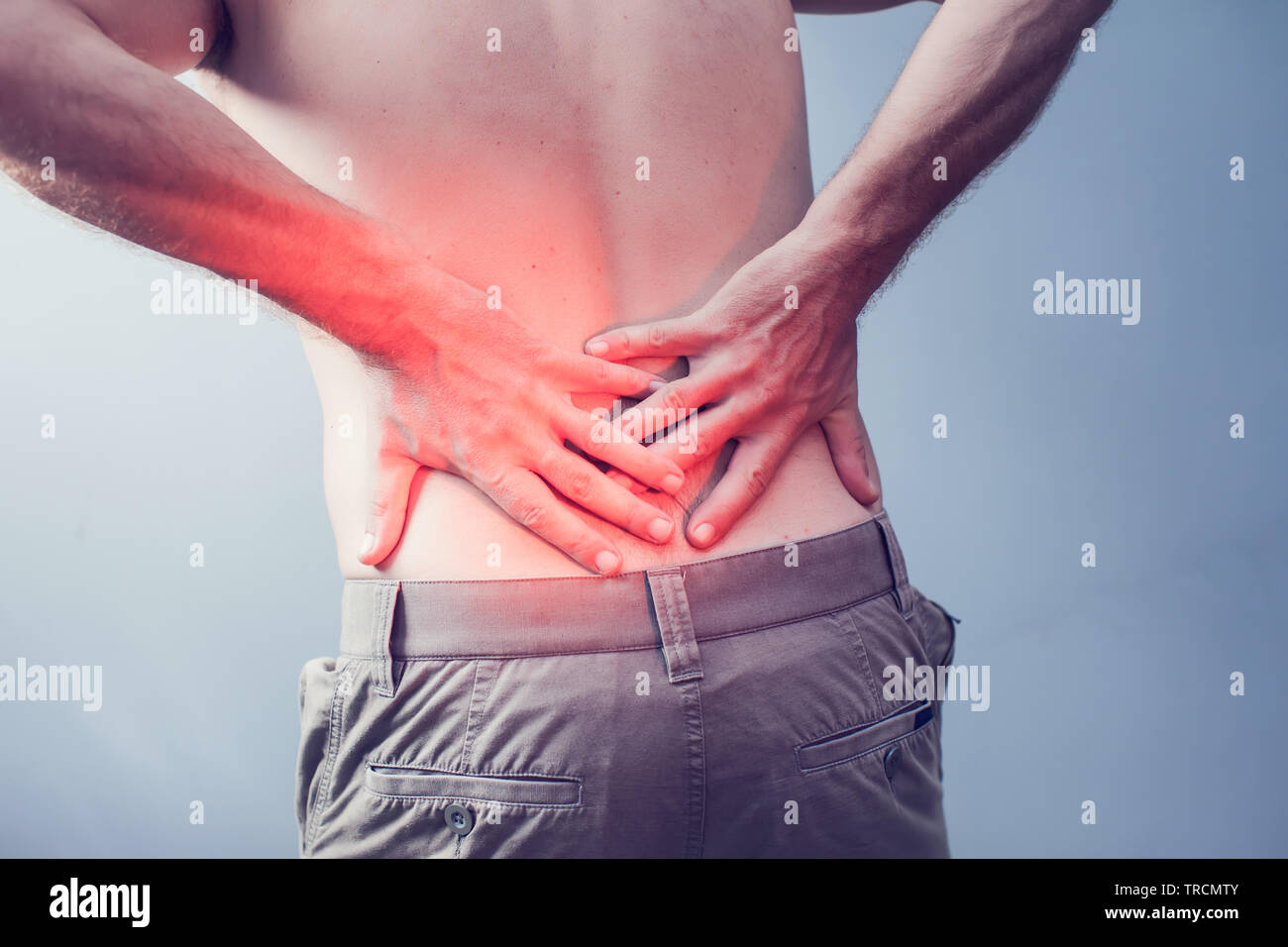 Lumbago symptom. Young man holding his painful inflamed loin. Health care and medicine. Stock Photo