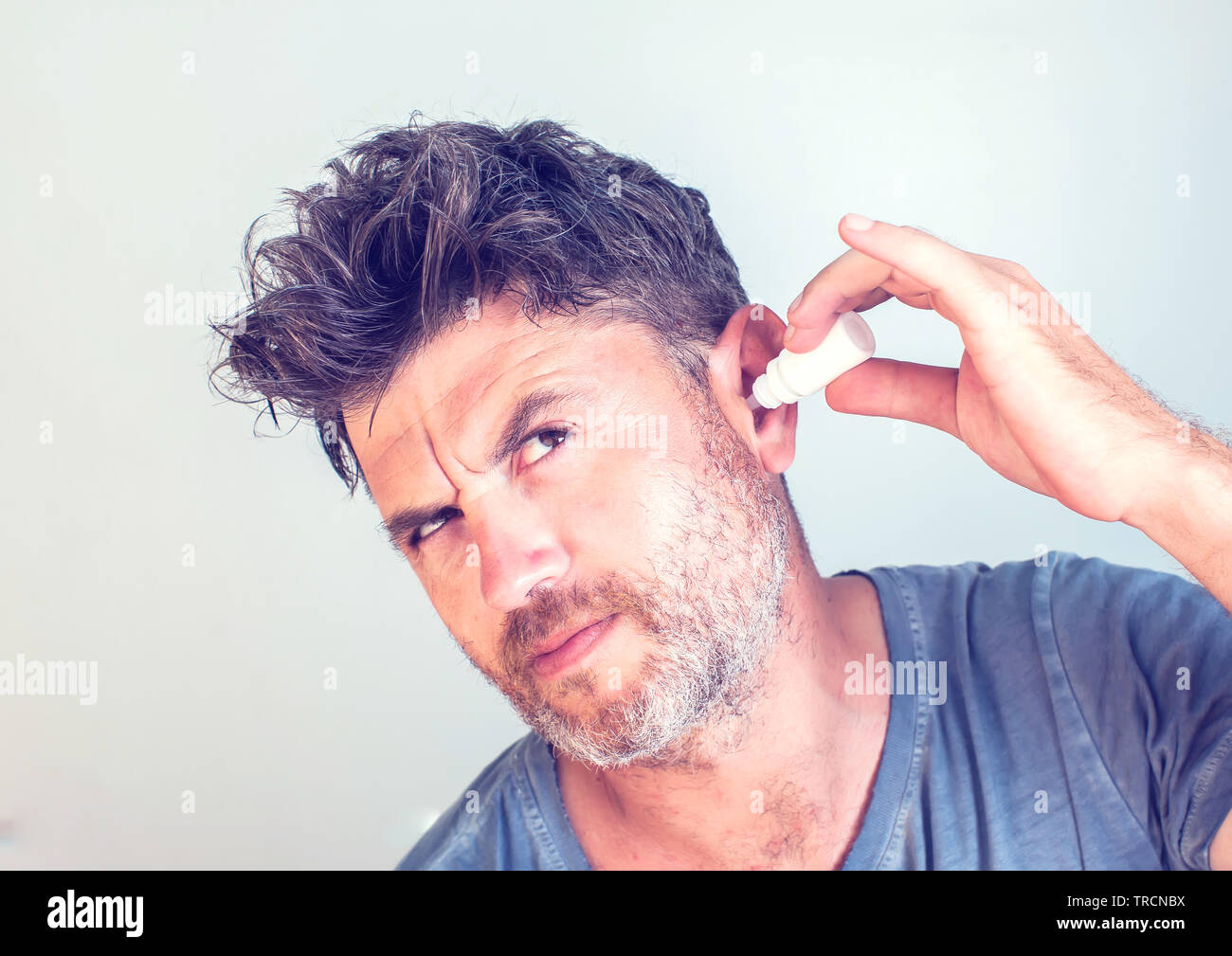 man using ear drops on gray background Stock Photo