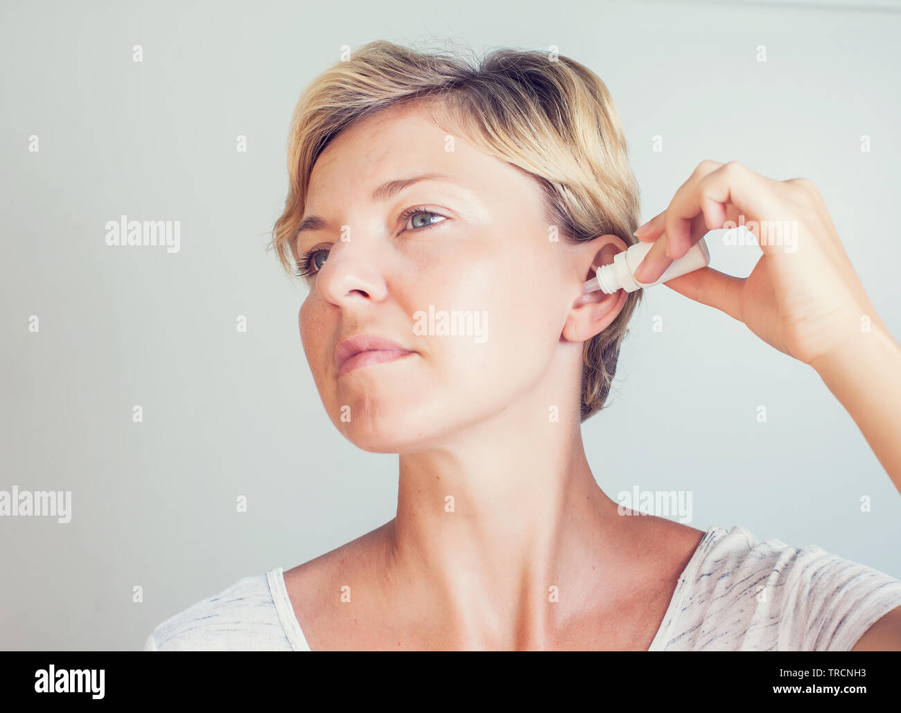 woman using ear drops on gray background Stock Photo