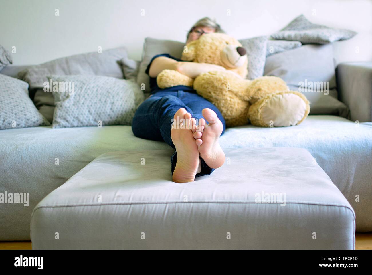 adult woman lying on sofa and holding teddybear in her arms Stock Photo