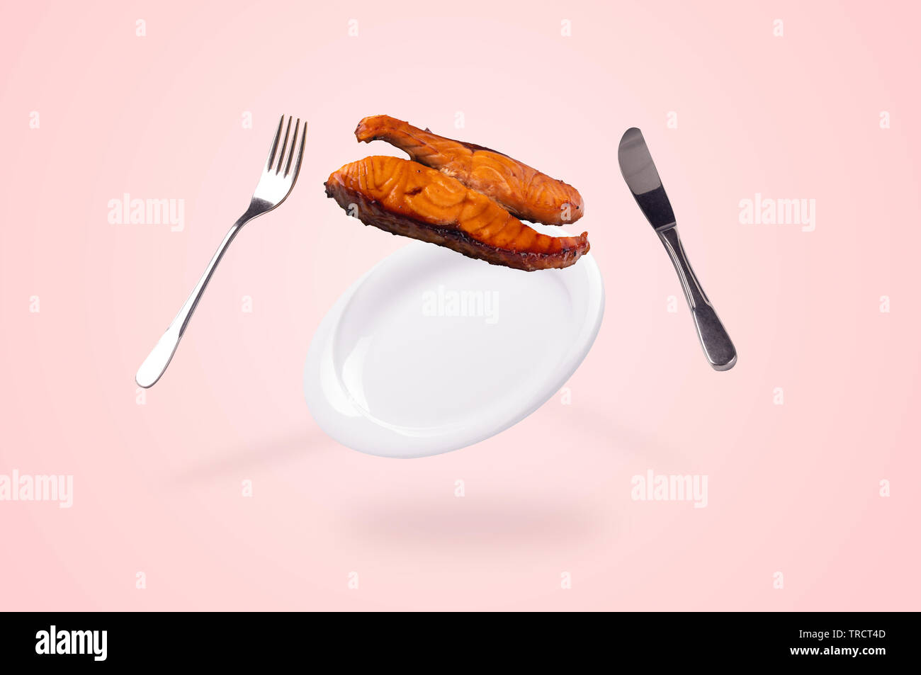grilled salmon fish falling on the levitating plate, fork and knife