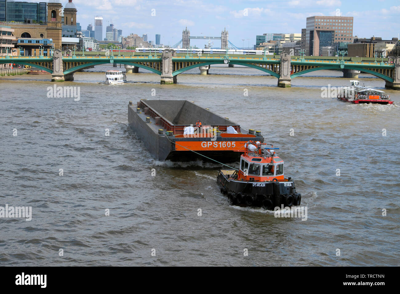View of tugboat towing barge & boats on River Thames, Southwark Bridge and Tower Bridge and city from Millennium Bridge London England UK KATHY DEWITT Stock Photo