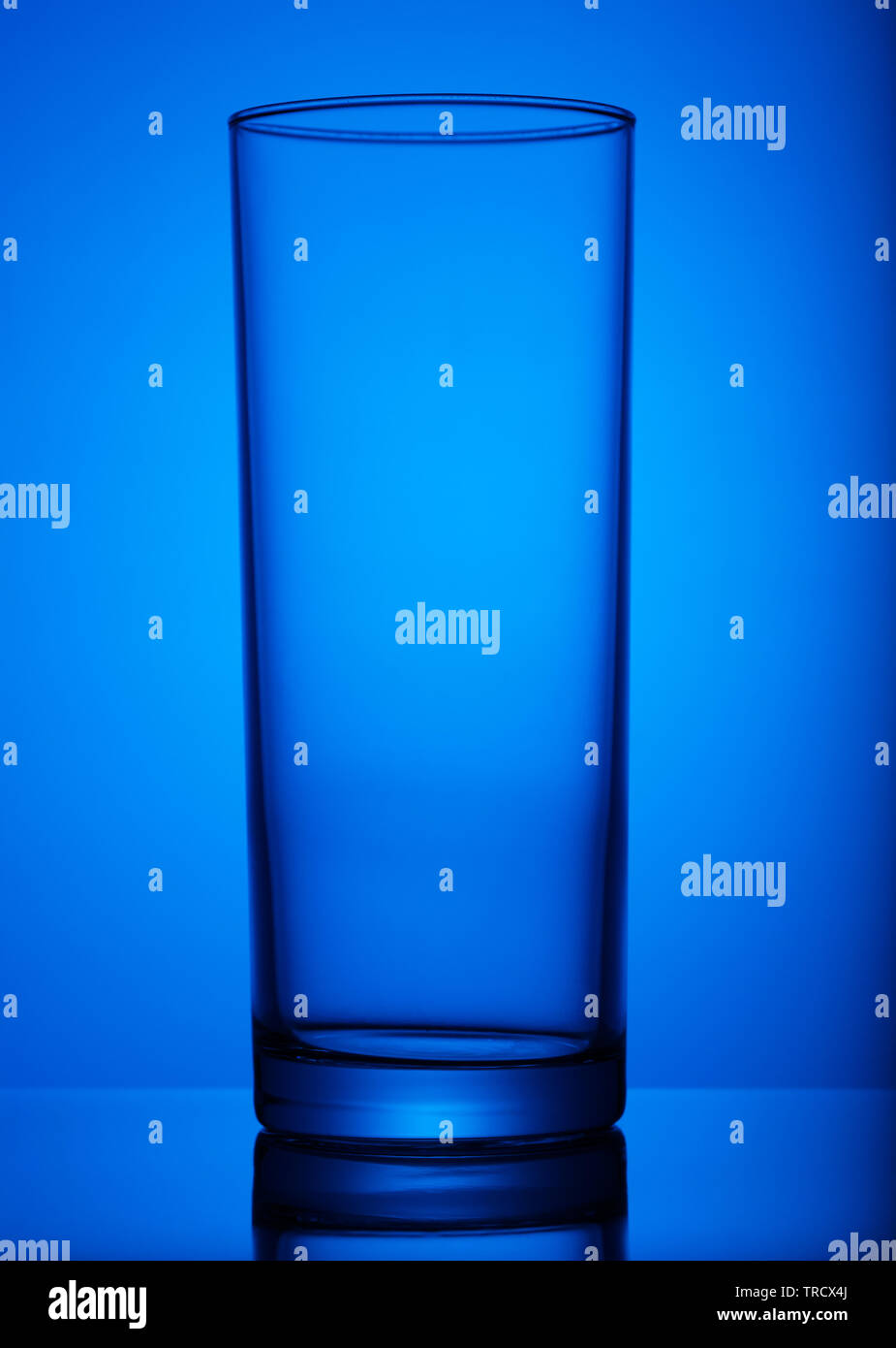 Transparent glass cup, shot in the light, with a vignette, on a blue background. art, subject, advertising. Stock Photo