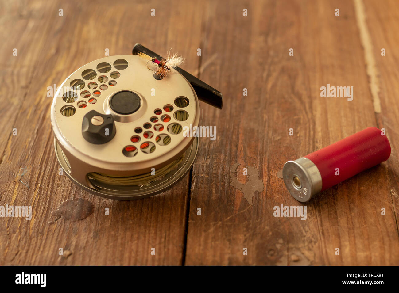Imag of  a Fly Fishing Reel, fly, And Shot Gun Catridge on Old Wood rusticTable Stock Photo