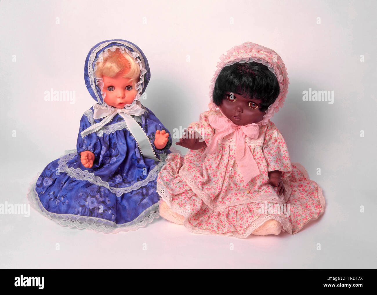 Black and white childrens toy doll wearing pretty dolls clothes sat together white studio background concept ideas image racial harmony & diversity Stock Photo