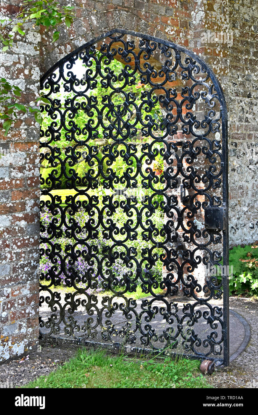 Old lockable heavy ornamental wrought iron gate on steel track open in arch brick wall opening giving access to walled garden country home England UK Stock Photo