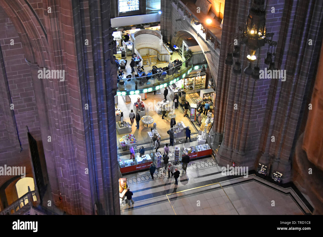 Looking down from high above on people shopping in gift shop & cafe inside nave of Liverpool Anglican cathedral with coloured wall lighting England UK Stock Photo