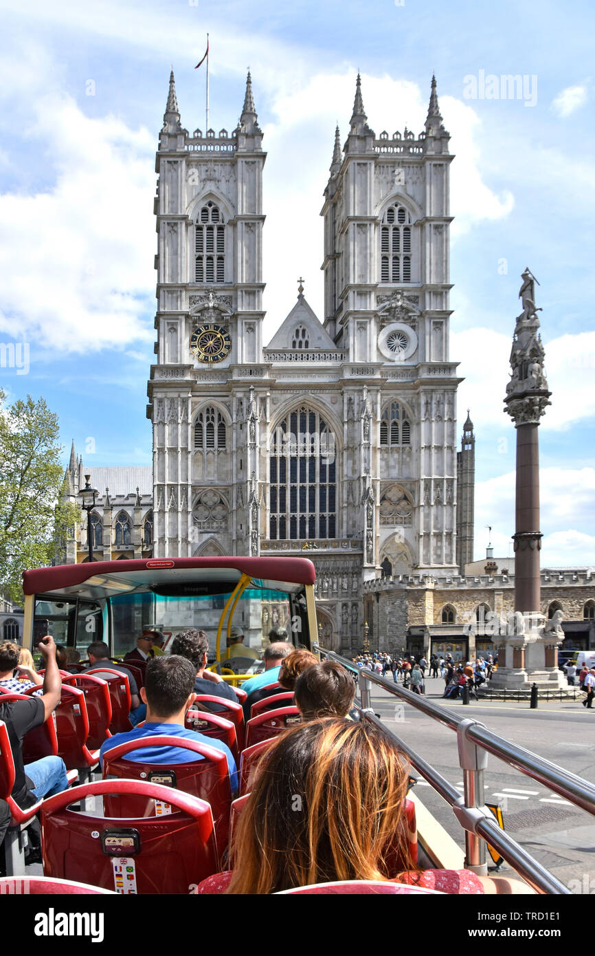 Open top double decker tourist bus passengers on summer sightseeing tour at west front Westminster Abbey with Scholars War Memorial column London UK Stock Photo
