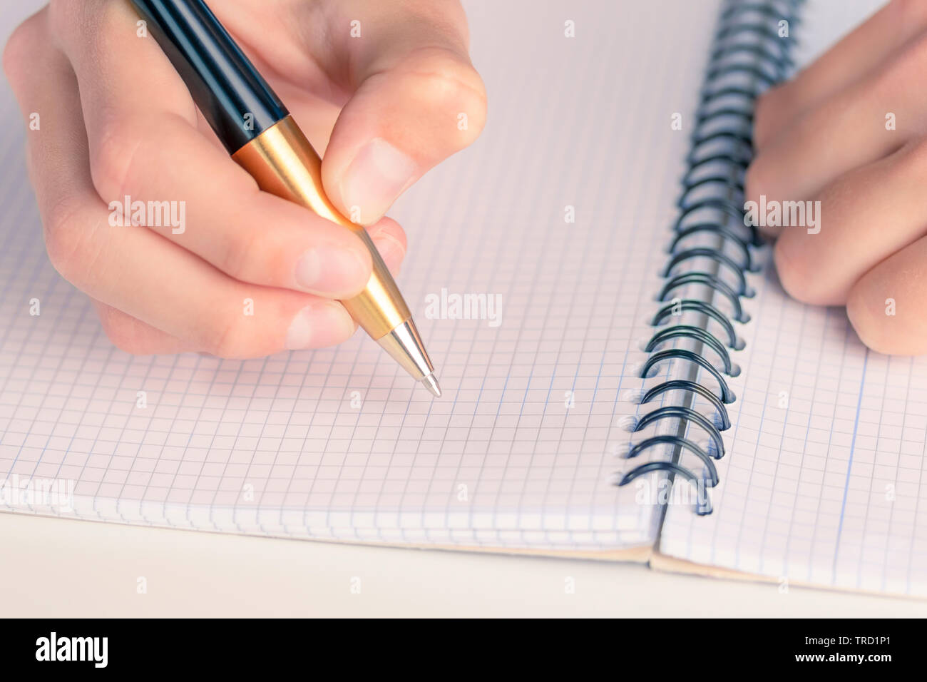 Man's hand with a black-gold pen over a clean sheet of checkered notebook. The concept of keeping a diary with a description of life events Stock Photo