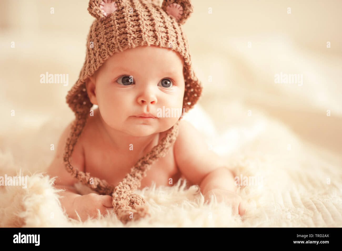 Cute baby girl wearing knitted hat lying in bed close up. Looking away. Childhood. Stock Photo
