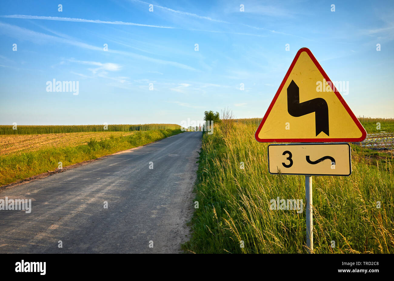 Dangerous bends traffic sign by a country road at sunset. Stock Photo