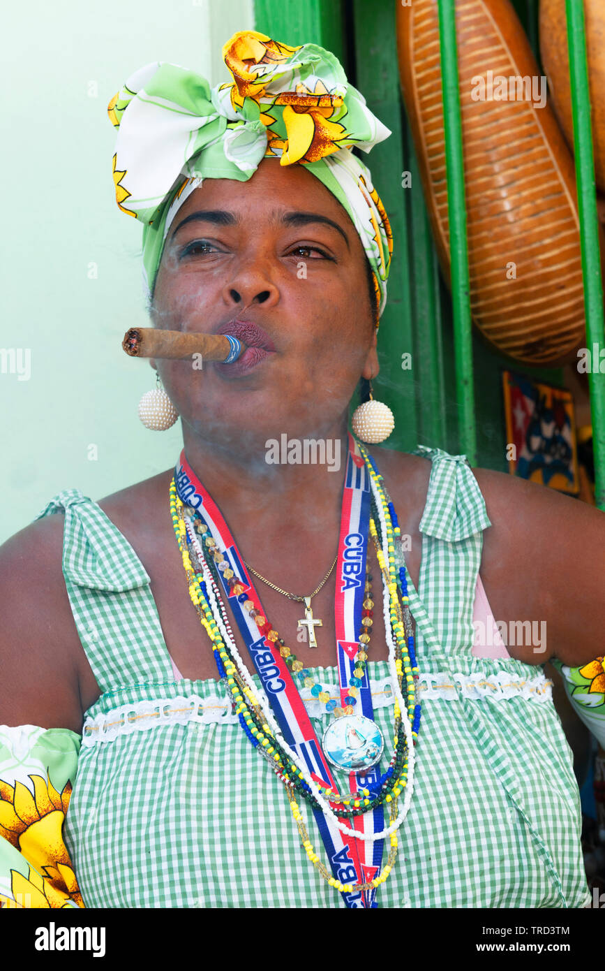 Colourfully dressed cuban lady sitting smoking a large cigar in one of the streets in the Old Town of Havana, Cuba, Caribbean Stock Photo