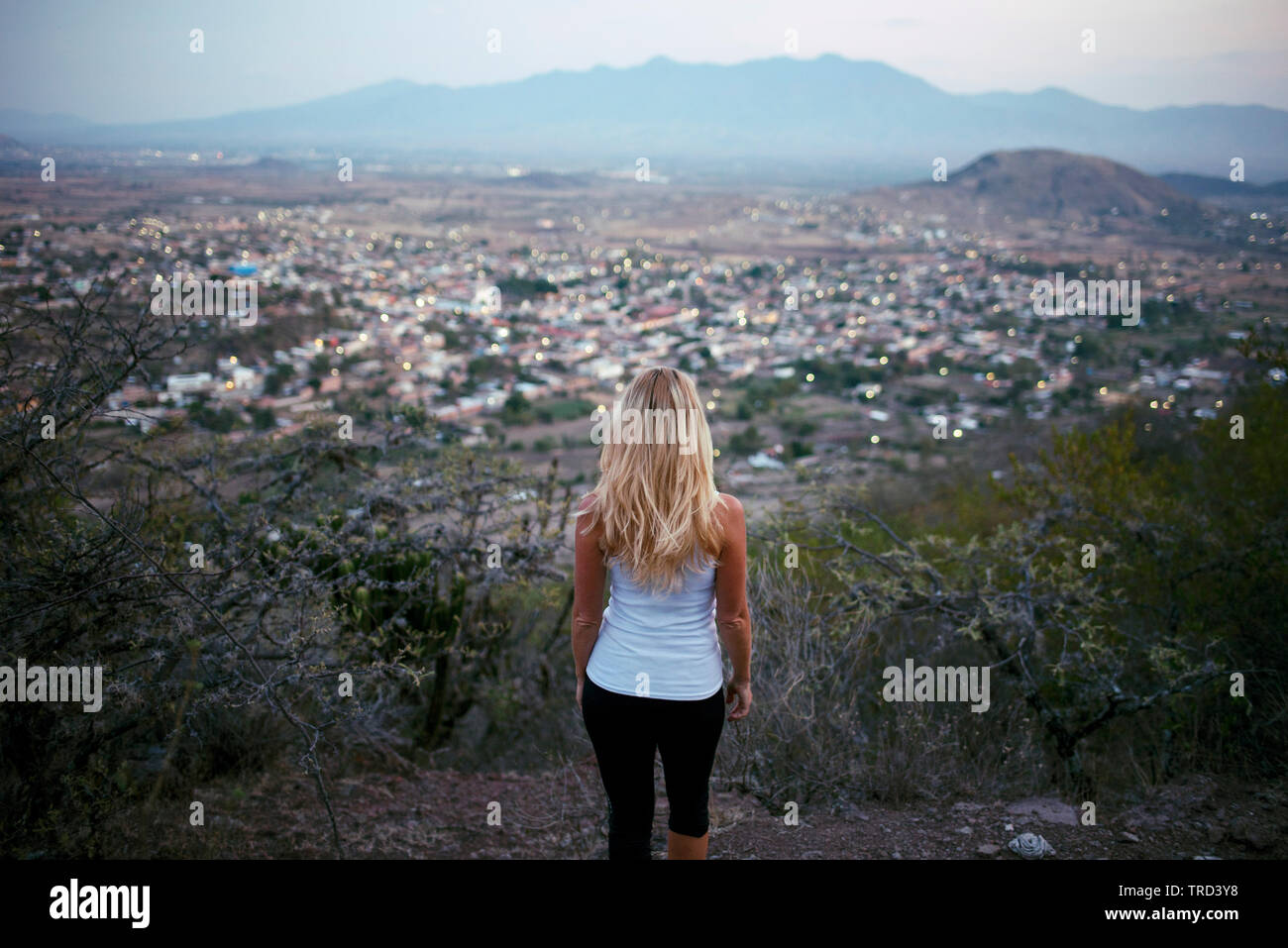 Blonde woman from behind looking at view standing above the town. Teotitlan del Valle, Oaxaca State, Mexico. May 2019 Stock Photo