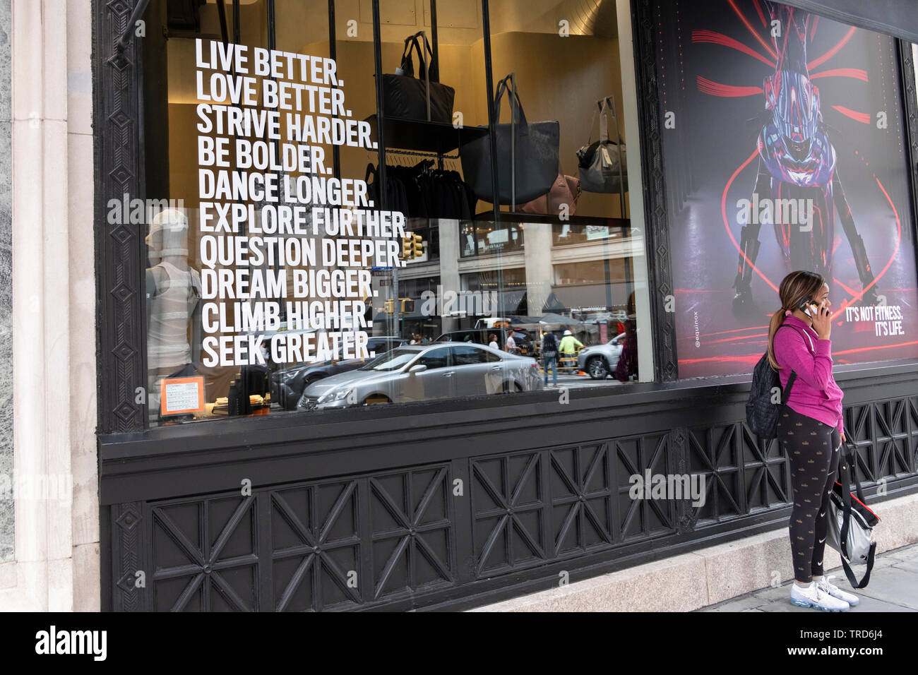 A woman on the phone outside an Equinox gym in Manhattan that has a most inspirational message in its window. Stock Photo