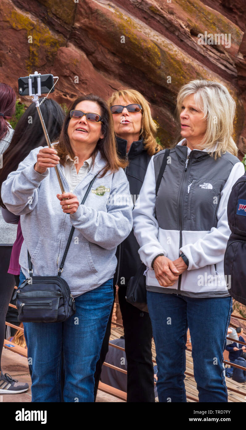 Three woman use a selfie stick to take their group photo with cell phone at Red Rocks Park Amphitheater near Morrison Colorado US. Photo taken in May. Stock Photo