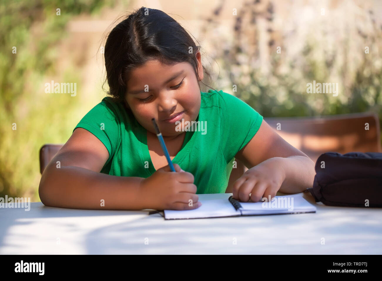 Smart elementary student using imagination to sketch ideas on notebook in an outdoor setting while the sun is setting. Stock Photo