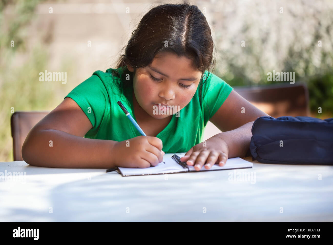 Focused young girl writing in her notebook, problem solving and studying outdoors in homeschool setting. Stock Photo