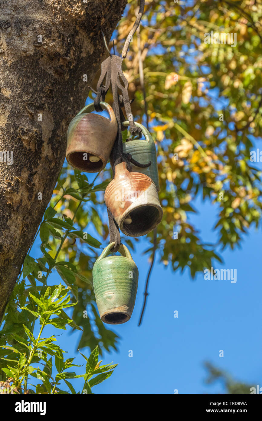 Ceramic cowbells hang in a tree with autumn leaves isolated against a