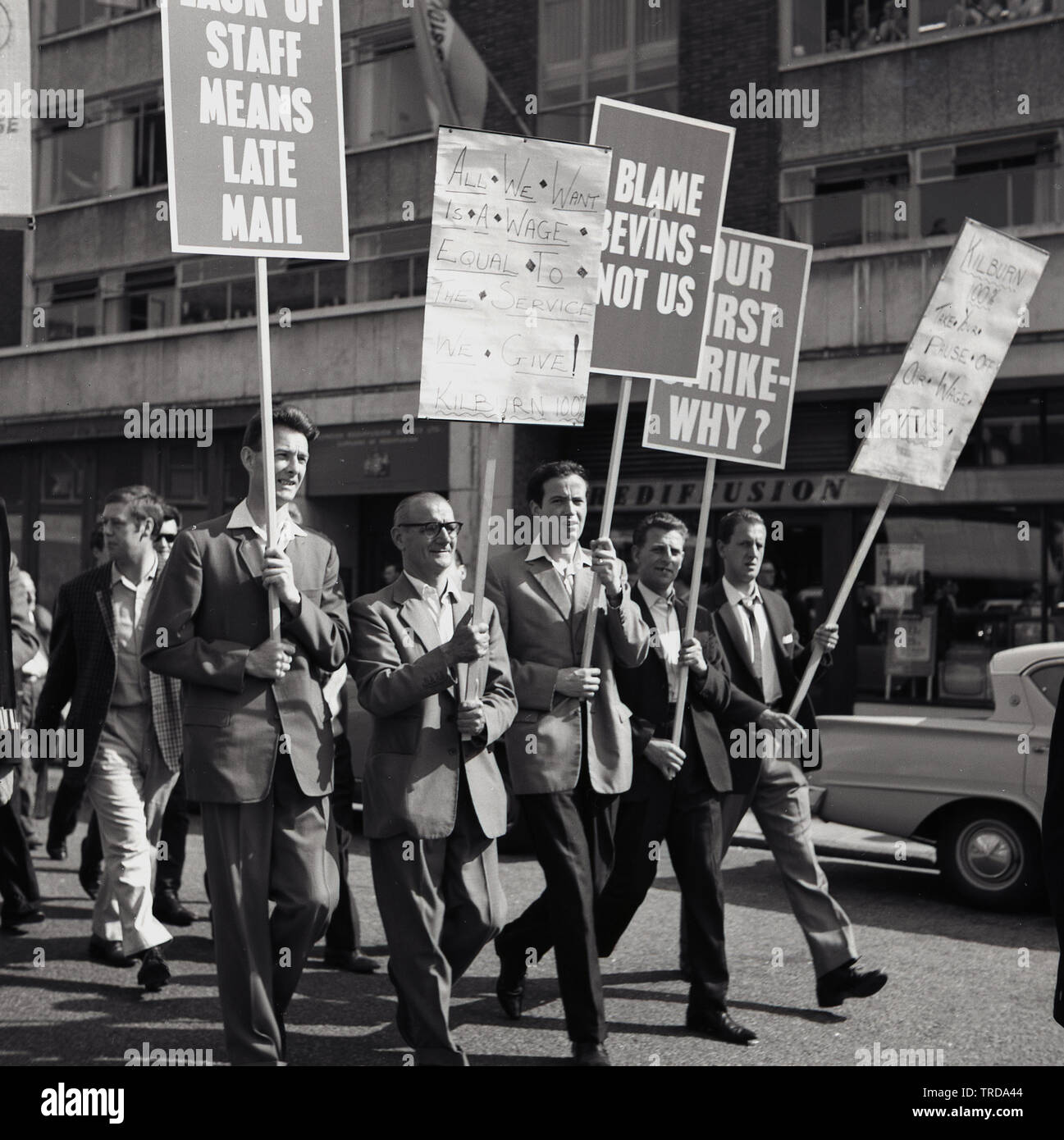 1960s, historical, striking Royal Mail postal workers walking through Central London holding placards, one saying...'Our first strike Why?  The postmen from the Kilburn branch were protesting about their low wages and demanding a fail deal on pay, with a particular angst with Ernest Bevin, the co-founder, in January 1922 - and former General Secretary - of the Transport and General Workers Union (TGWU) which had become Britain's largest trade union. Stock Photo