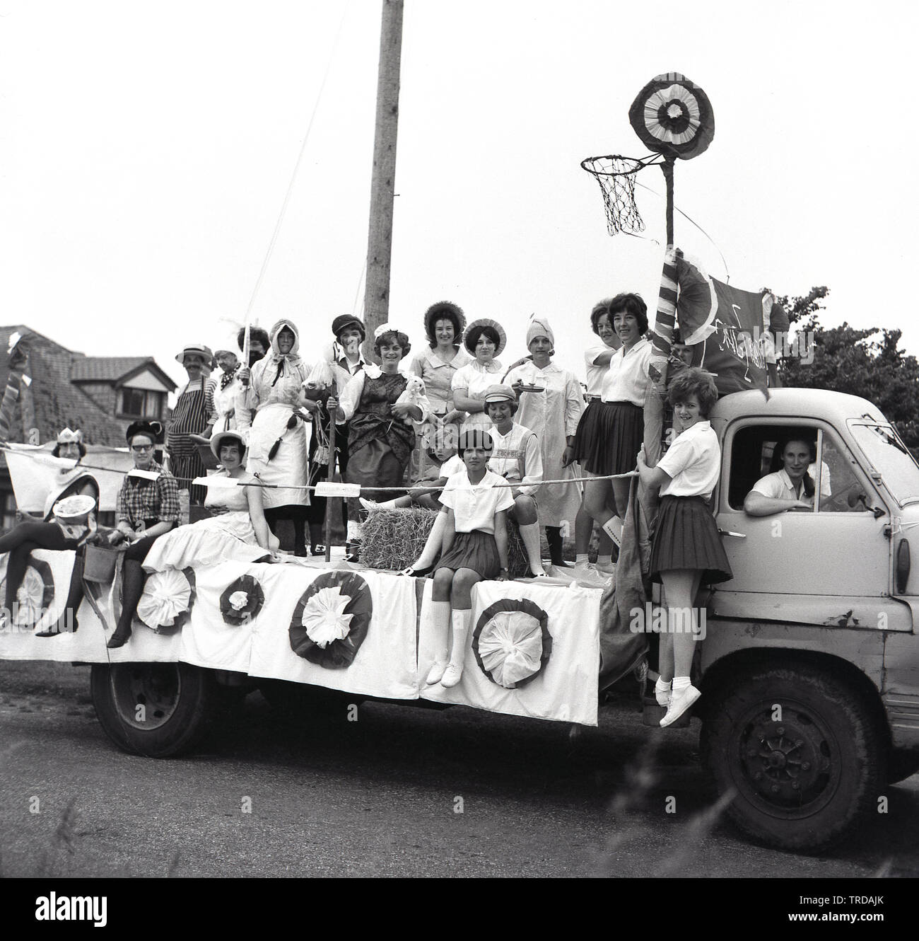 1967, historical, a group of people on a decorated float on the back of a truck dressed in different fancy dress taking part in a carnival or fete. Several of the females are  in school PE kit and there is a net attached and so a theme of school days and netball. Stock Photo