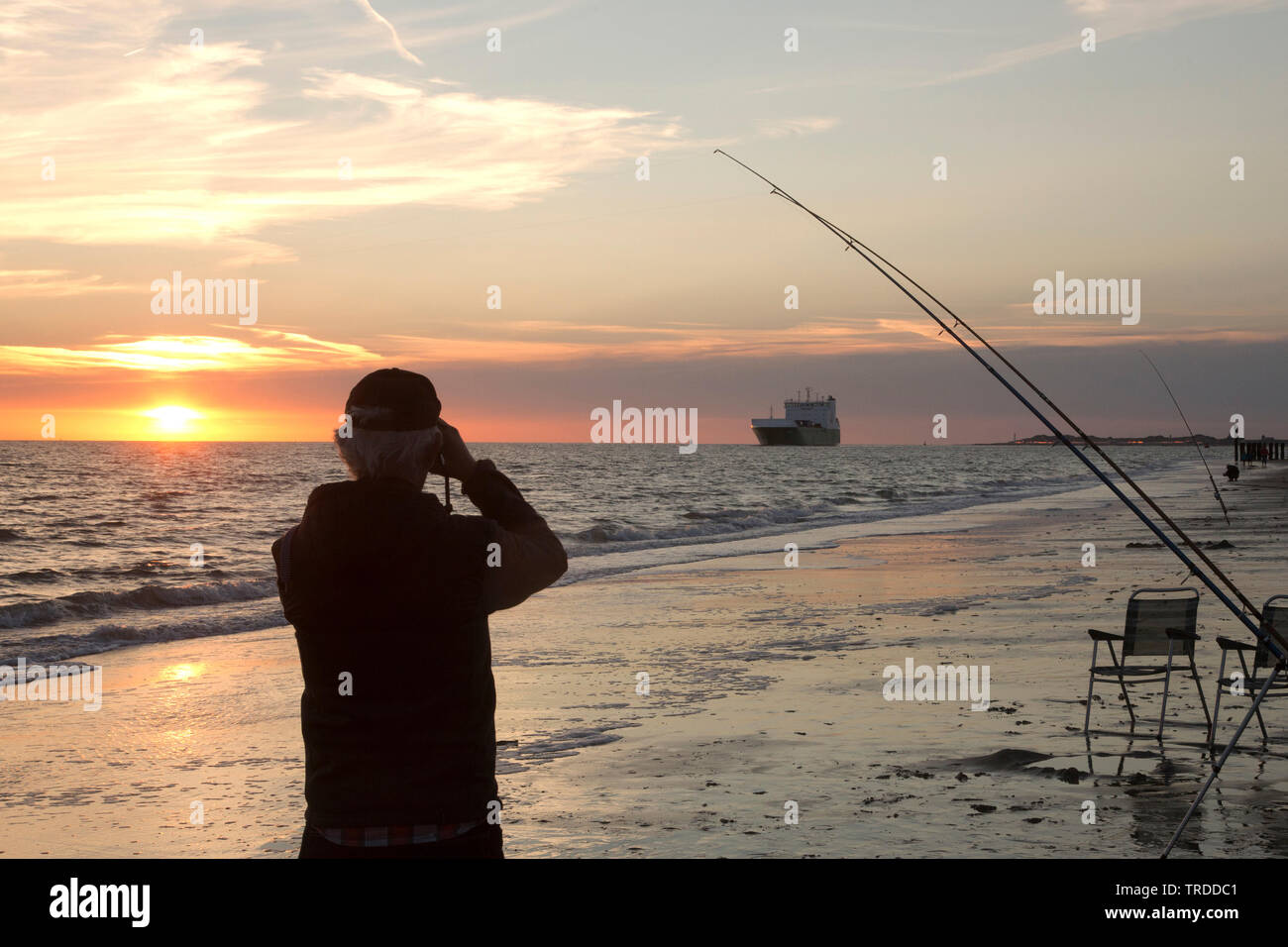 recreational fisherman on the beach looking through the binocular to a ship, Netherlands Stock Photo