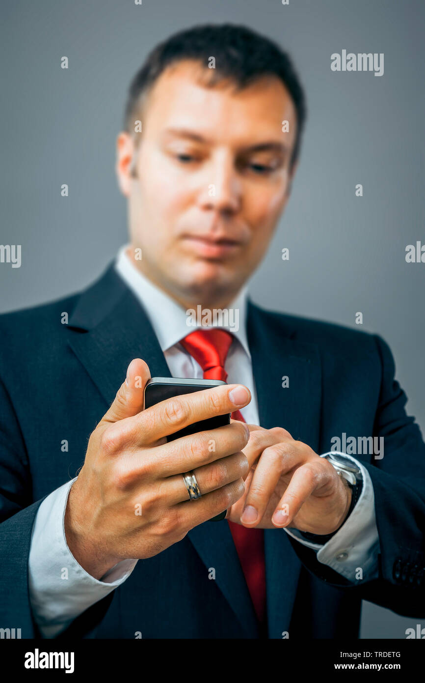 Portrait of a likeable Businessman in a black suit using a smartphone against grey background Stock Photo