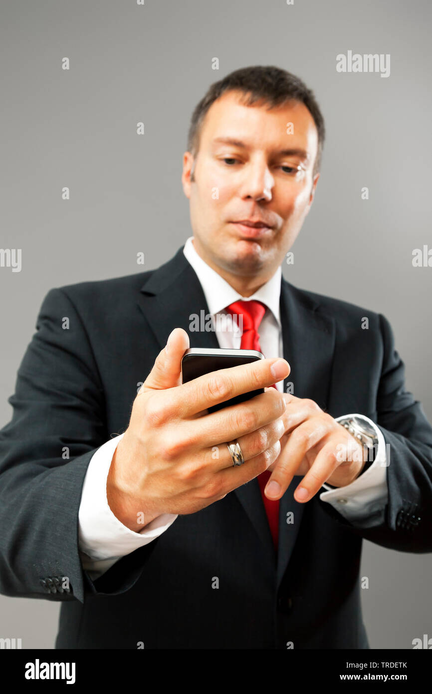 Portrait of a likeable Businessman in a black suit using a smartphone against grey background Stock Photo