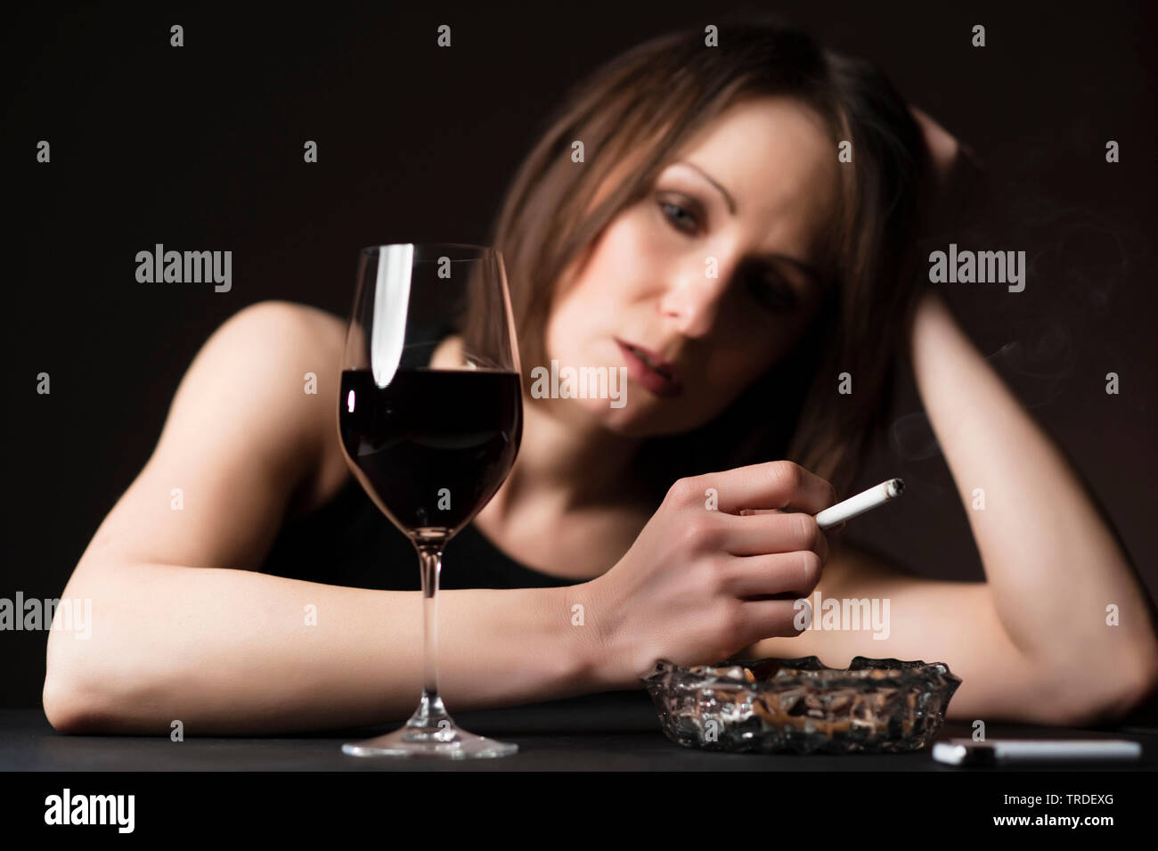 Portrait of a depressed and alcoholised woman with a glass of wine and a cigarette in her hands Stock Photo