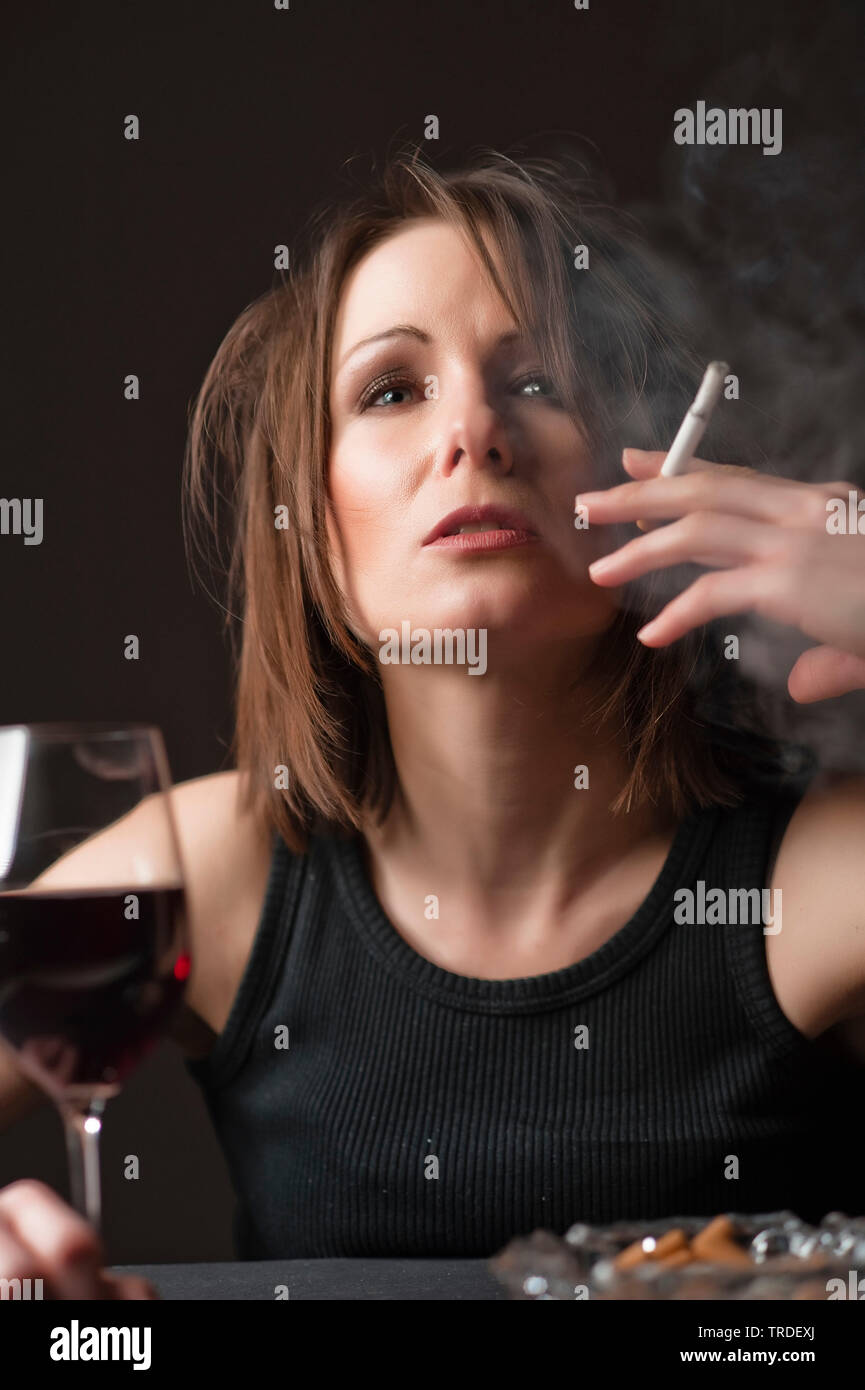 Portrait of a depressed alcoholised woman with a glass of wine and a cigarette in her hands Stock Photo