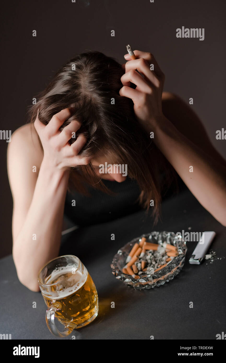 Portrait of a depressed and alcoholised woman with a glass of  beer and a cigarette in her hands Stock Photo