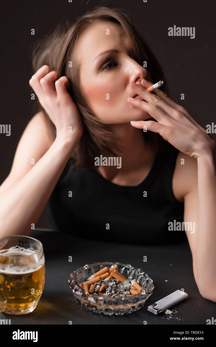 Portrait of a depressed and alcoholised woman with a glass of  beer and a cigarette in her hands Stock Photo