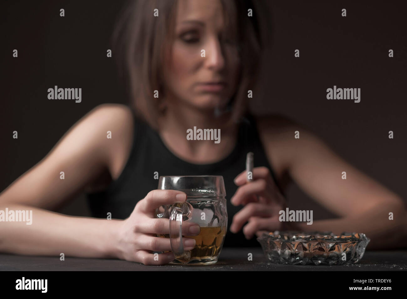 Portrait of a depressed and alcoholised woman with a glass of  beer and a cigarette in her hands Stock Photo