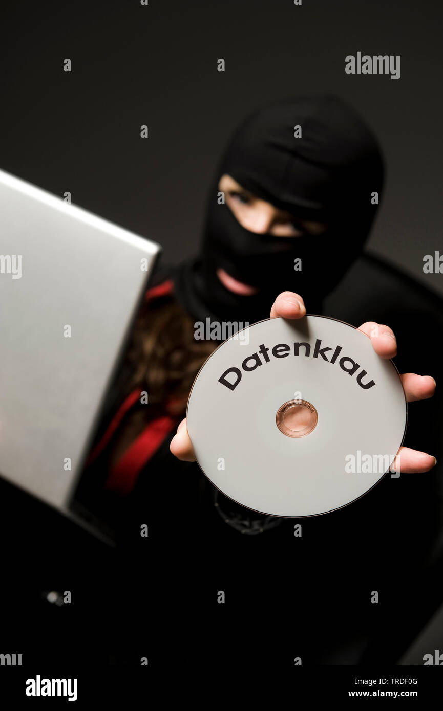 Portrait of an Business woman wearing a ski mask holding laptop and CD lettering DATENKLAU (data theft) / Cybercrime Stock Photo