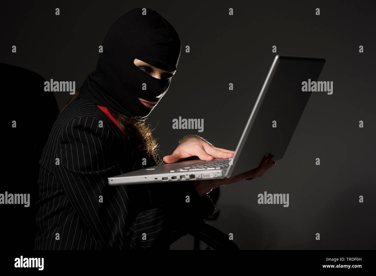 Portrait of an attractive Business woman wearing a ski mask and working with a laptop / Cybercrime Stock Photo