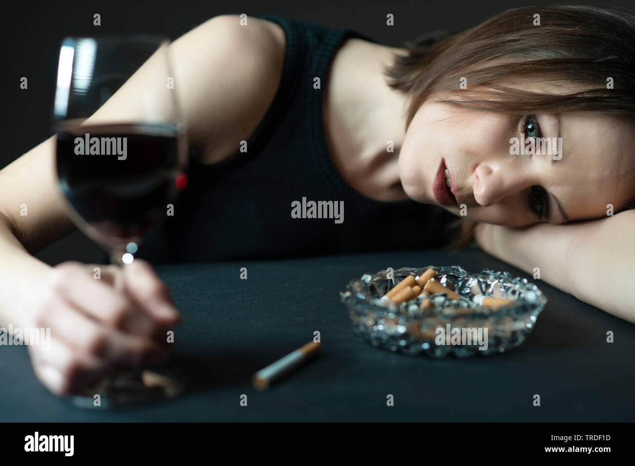Portrait of a depressed and alcoholised woman holding a glass of wine with cigarettes in front of her Stock Photo