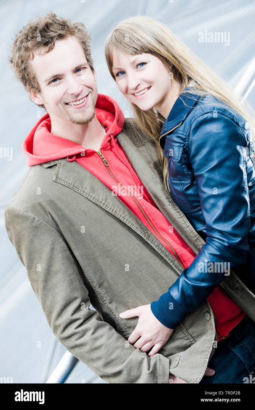 Portrait of a young couple hugging and smiling into the camera outdoors ...