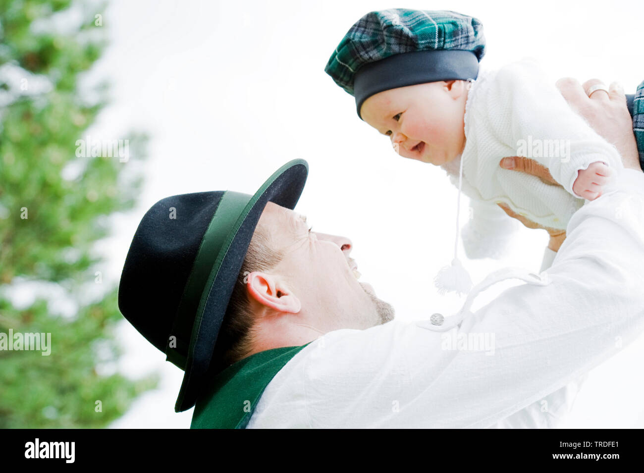 Portrait of a young man dressed in traditional costume holding up a baby, Germany, Bavaria Stock Photo