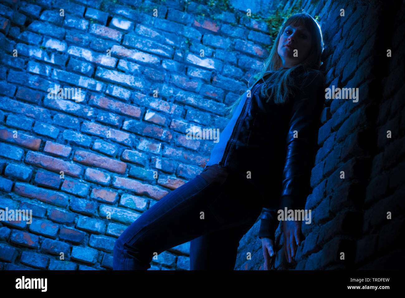 Night shot of a woman dressed in jeans and blue t-shirt in front of red brick walls Stock Photo