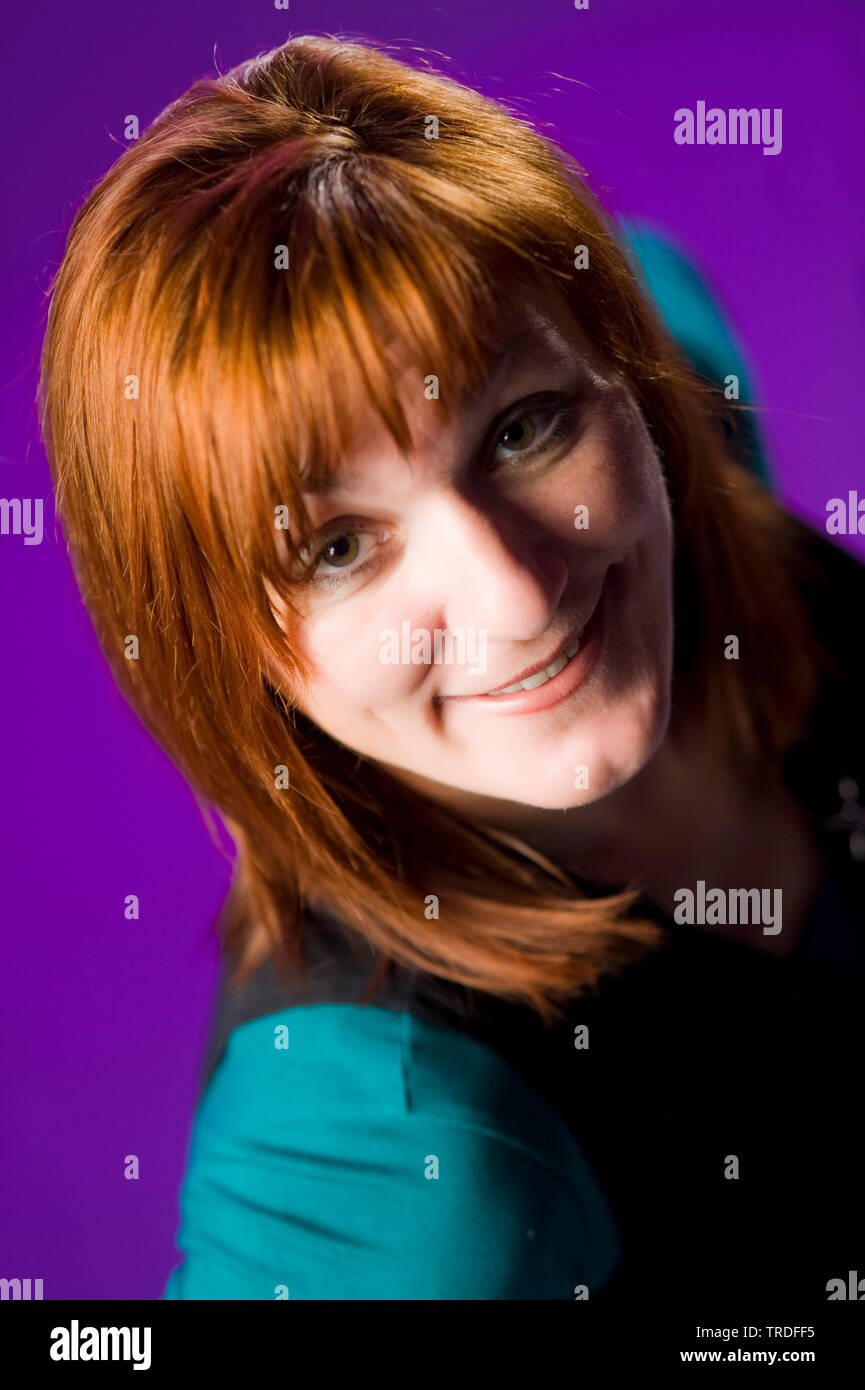 Portrait of a likeable middle aged woman with red hair against purple background Stock Photo