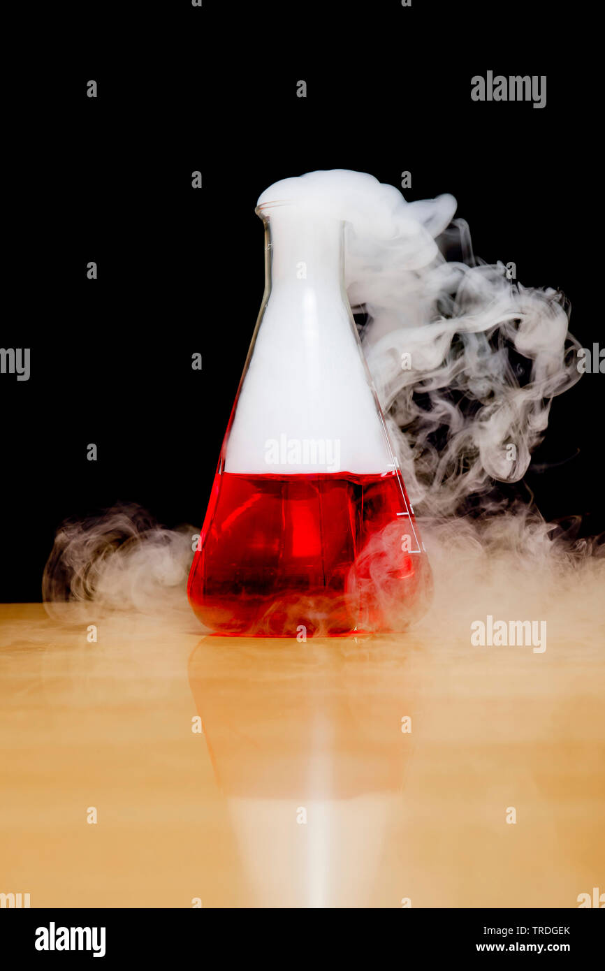 Erlenmeyer flask filled with red liquid and white vapor against black background Stock Photo