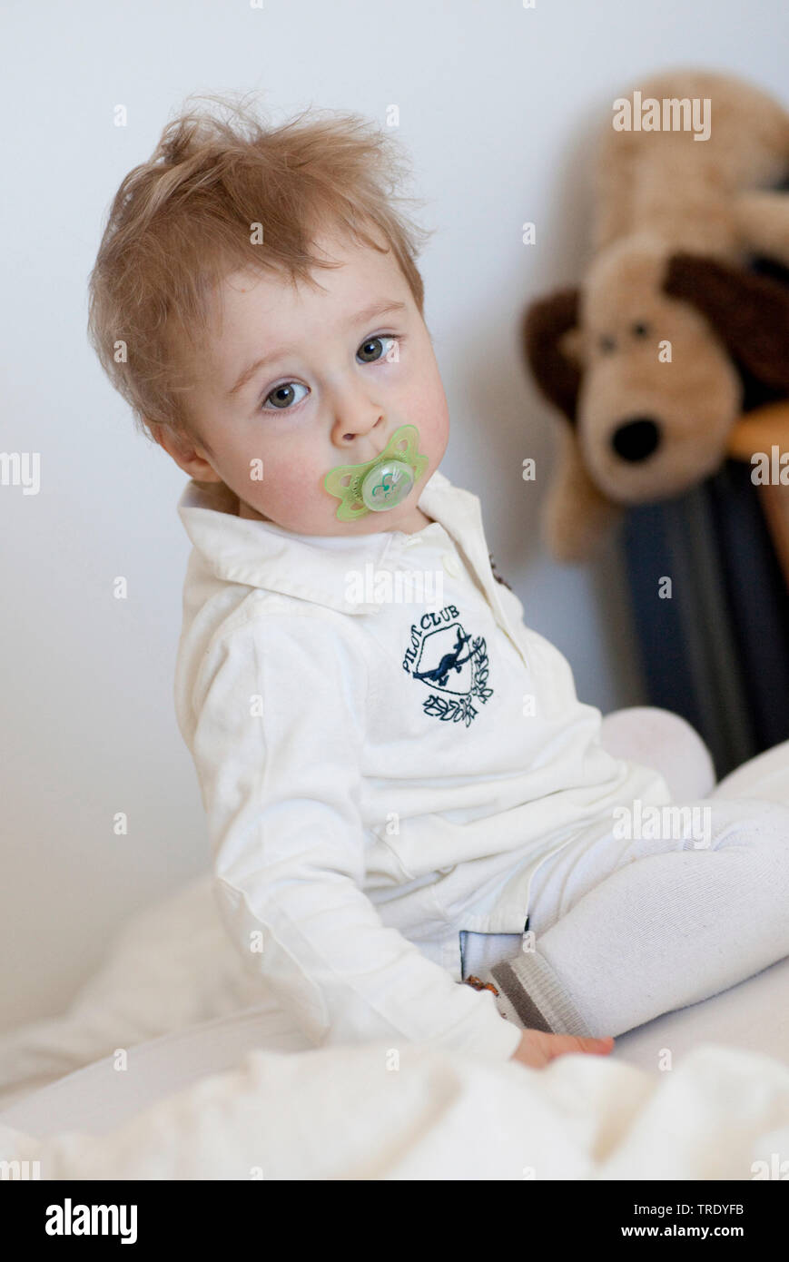 Portrait of a young boy with comforter looking into the camera with a stuffed animal in the background Stock Photo