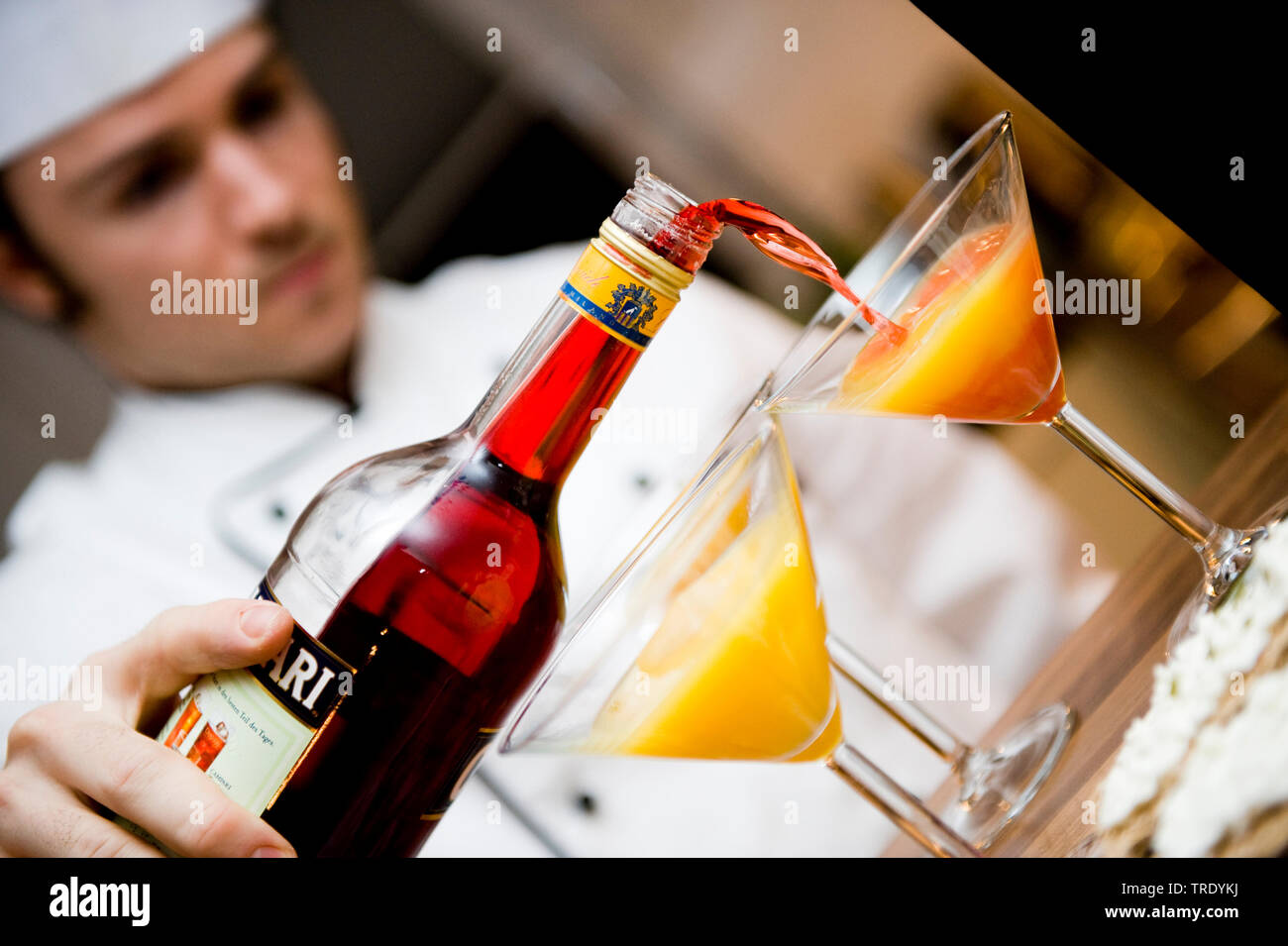 Waiter fills a cocktail glass of orange juice with Campari Stock Photo