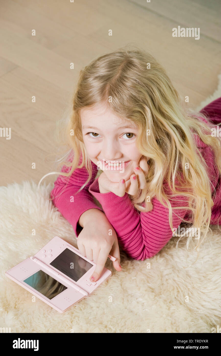 Portrait of a girl lying on the floor and playing with her Nintendo console Stock Photo