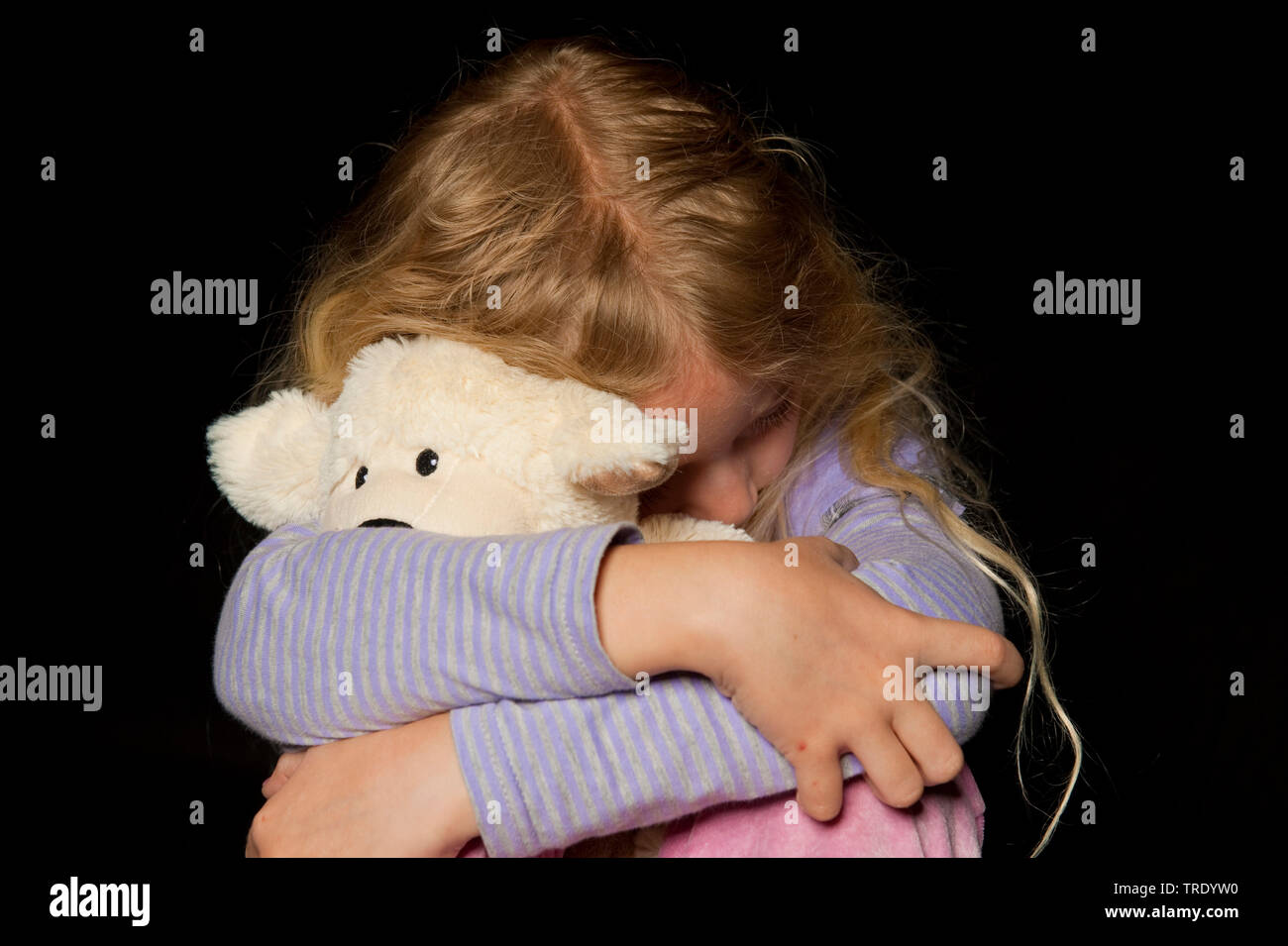 Portait of a young girl, hidding her head behind a stuffed animal - child abuse Stock Photo