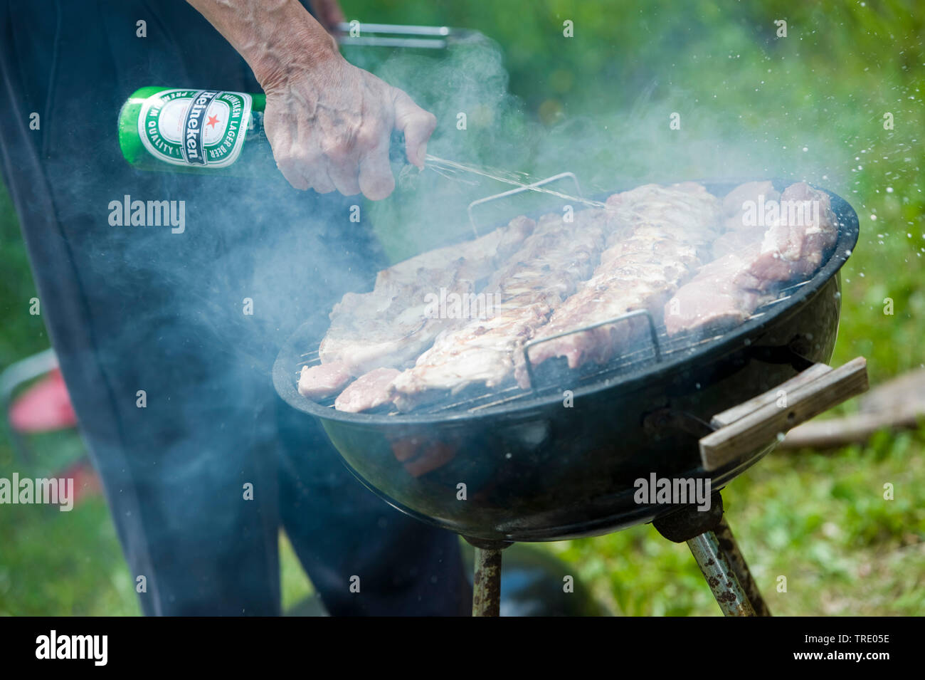 Meat on a charcoal barbecue deglazing with beer Stock Photo