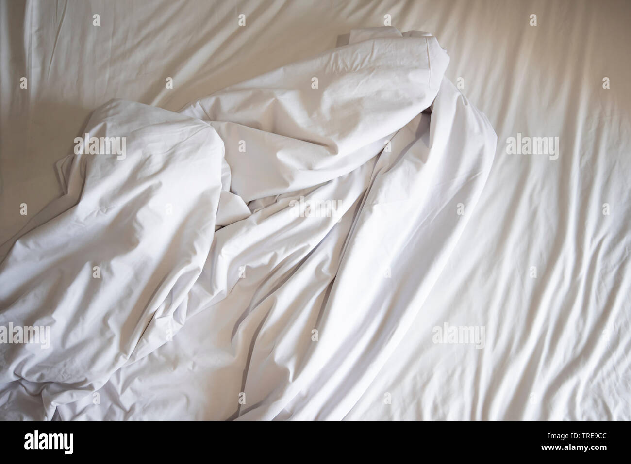 Unmade bed sheet of the crease and white blanket in the bedroom after