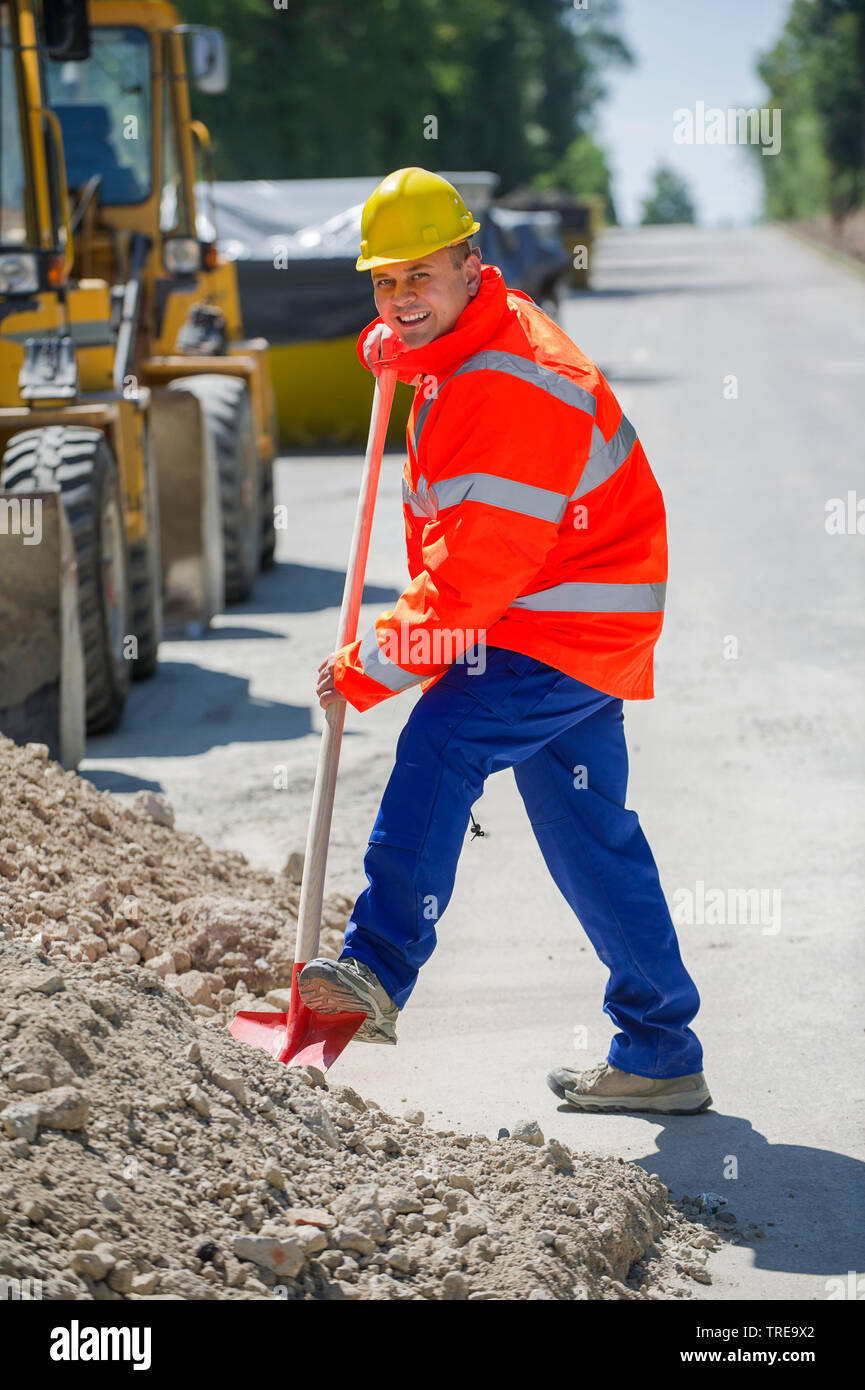 Construction worker in a orange high-visibility jacket, shoveling sand on a road Stock Photo